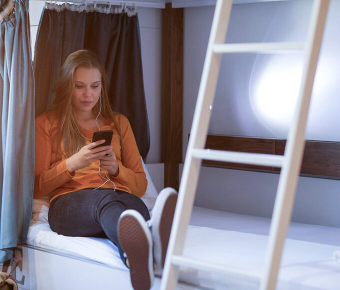 Alleinreisende Frau mit Smartphone in einem Hostelzimmer