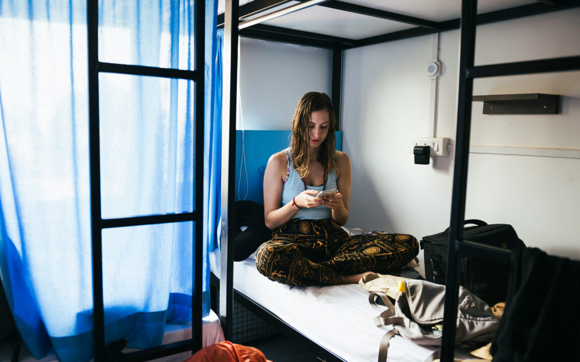 Alleinreisende Frau sitzt auf einem Etagenbett in einem Mehrbettzimmer eines Hostels.