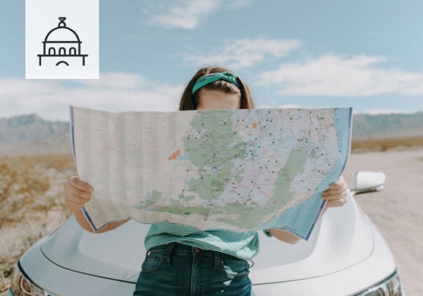 Alleinreisende Frau mit Straßenkarte vor einer europäischen Landschaft